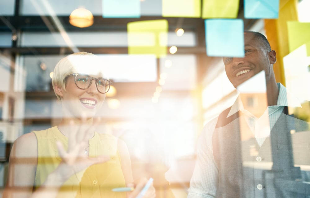 Two creative millenial small business owners working on social media strategy brainstorming using adhesive notes in windows-1