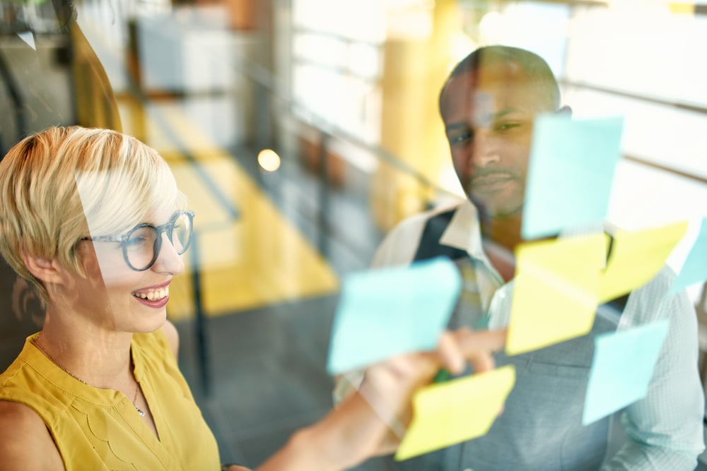 Two creative millenial small business owners working on social media strategy brainstorming using adhesive notes in windows-2