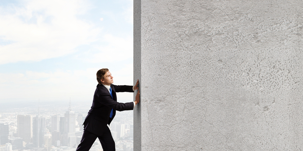 Young businessman making effort to move stone wall